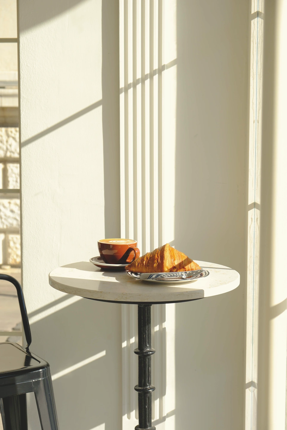 Café y croissant junto a una pared iluminada por el sol con estampado envejecido