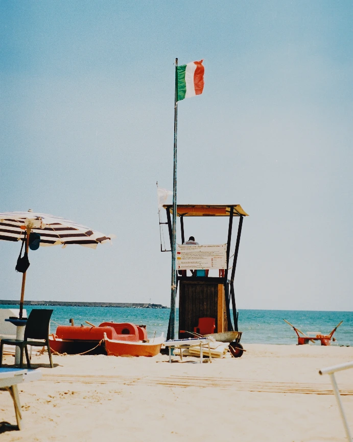 An Italian beach with a lifeguard tower, red boat, and pale blue sky — Gold 200
