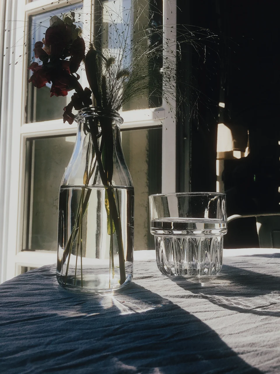 Blumen und ein Glas Wasser im Sonnenlicht am Fenster, mit Window Light