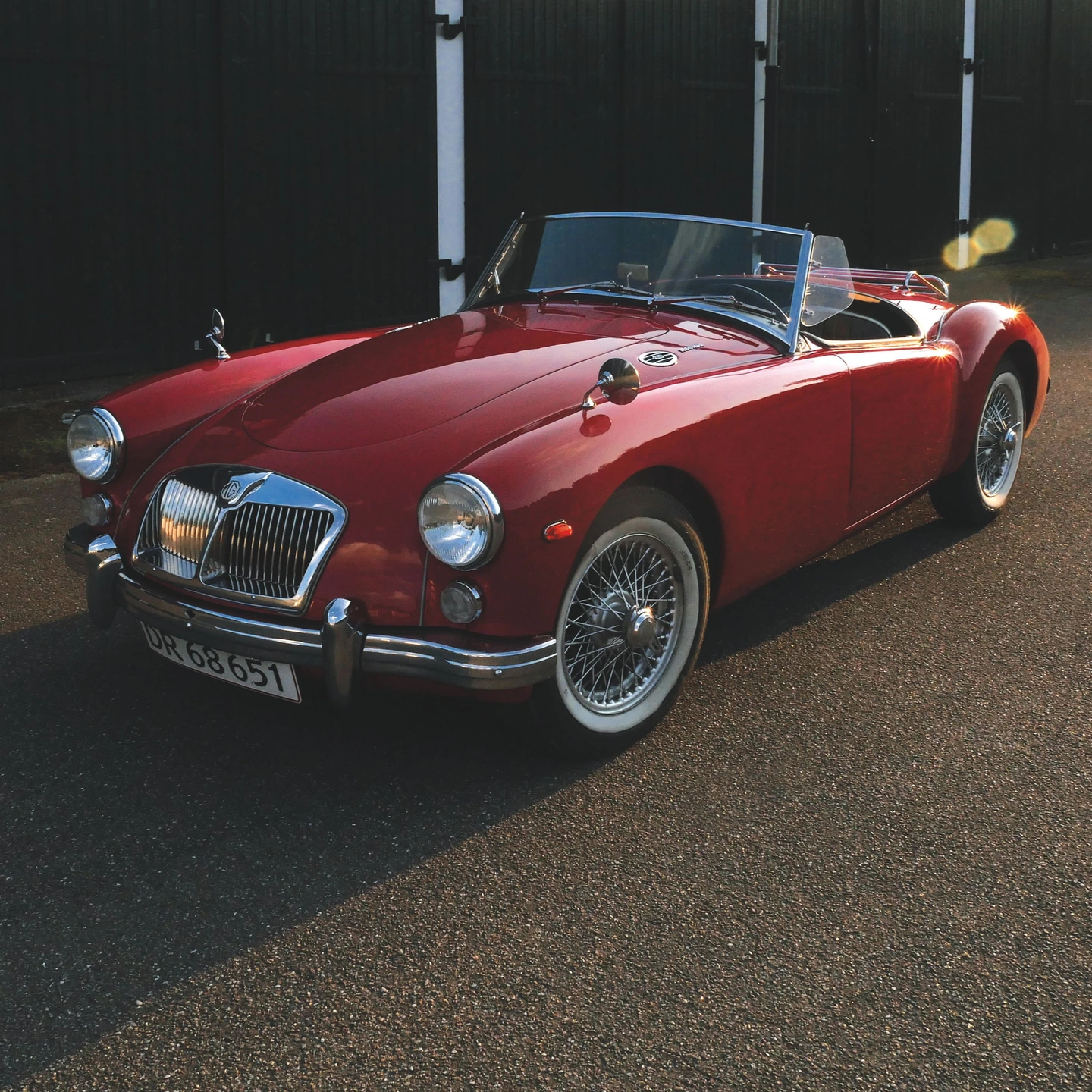 Square crop concentrating on a red vintage roadster and its surroundings