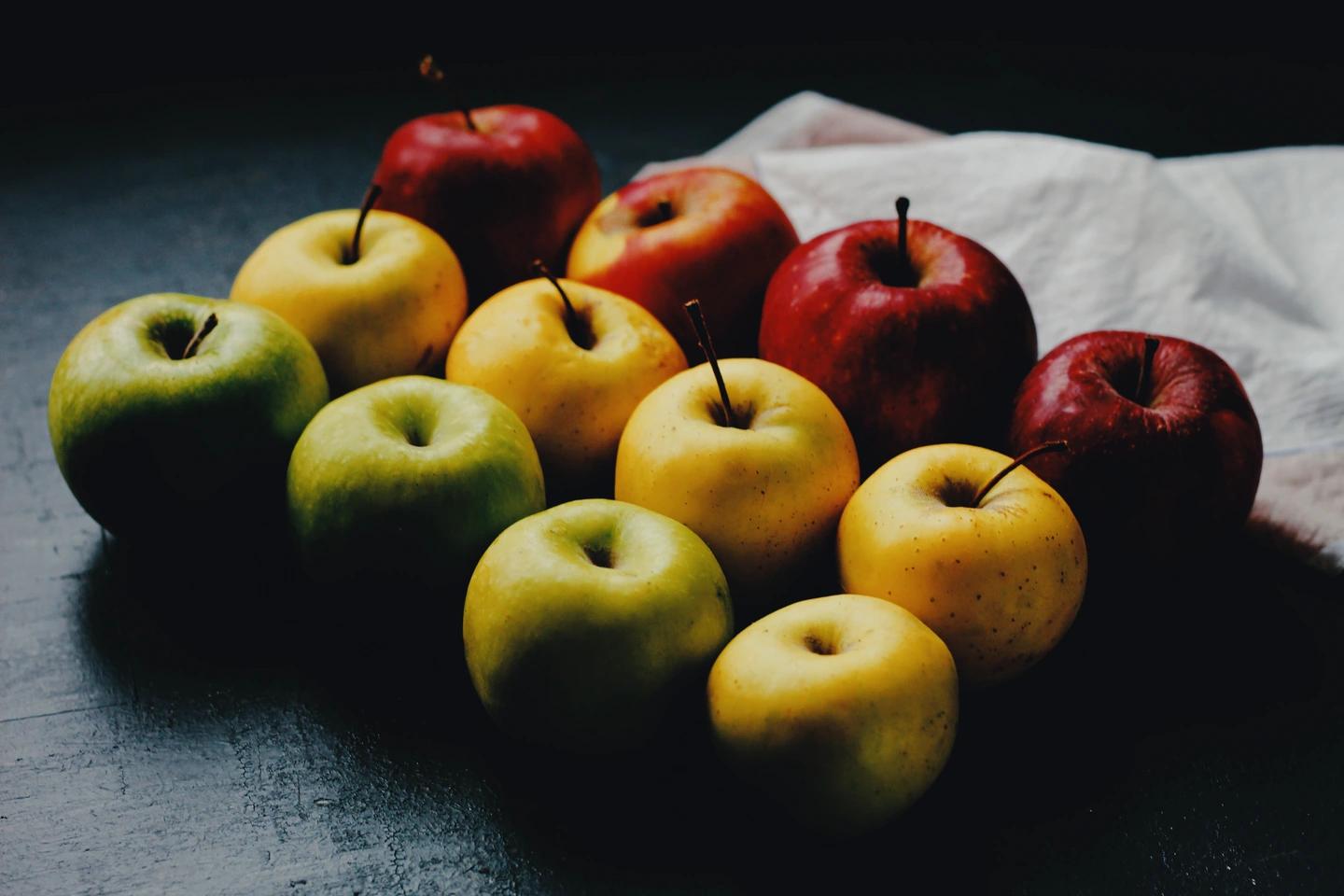 Red, green and yellow apples beside a white cloth, with a daylight film treatment