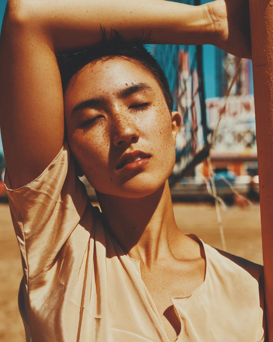A freckled woman shading her face with her arm in the sun, with the Faded Summer preset in Photonica
