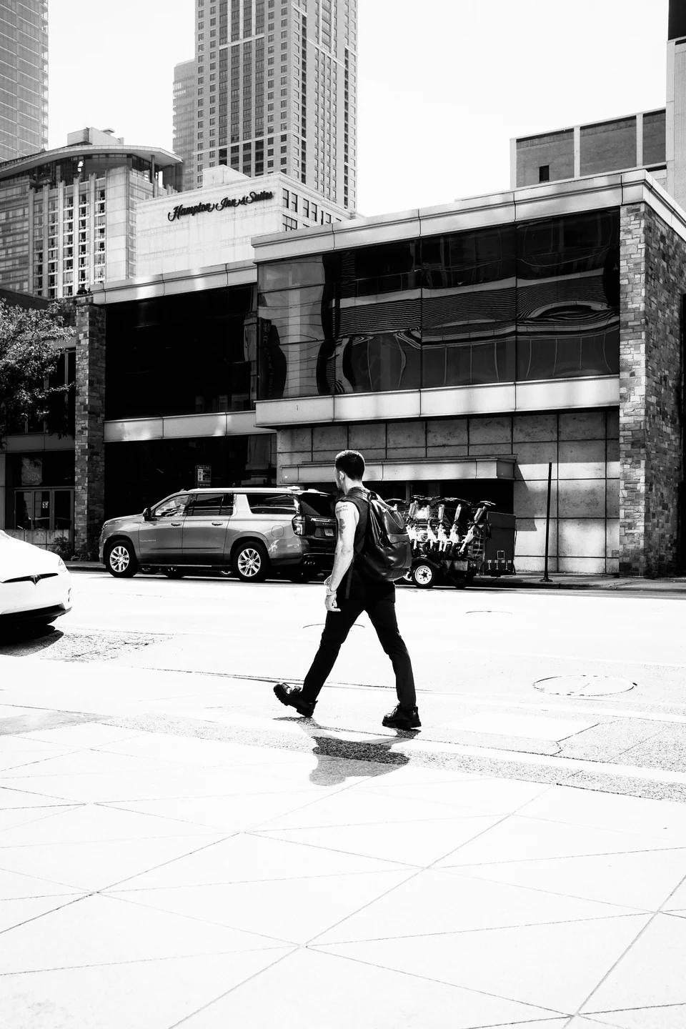 A pedestrian crossing a city street in hard sunlight, with the Ink preset in Photonica