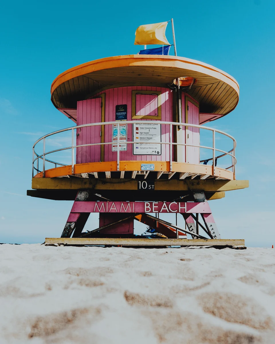 A pink and yellow lifeguard tower against a blue Miami sky, with the Postcard preset in Photonica